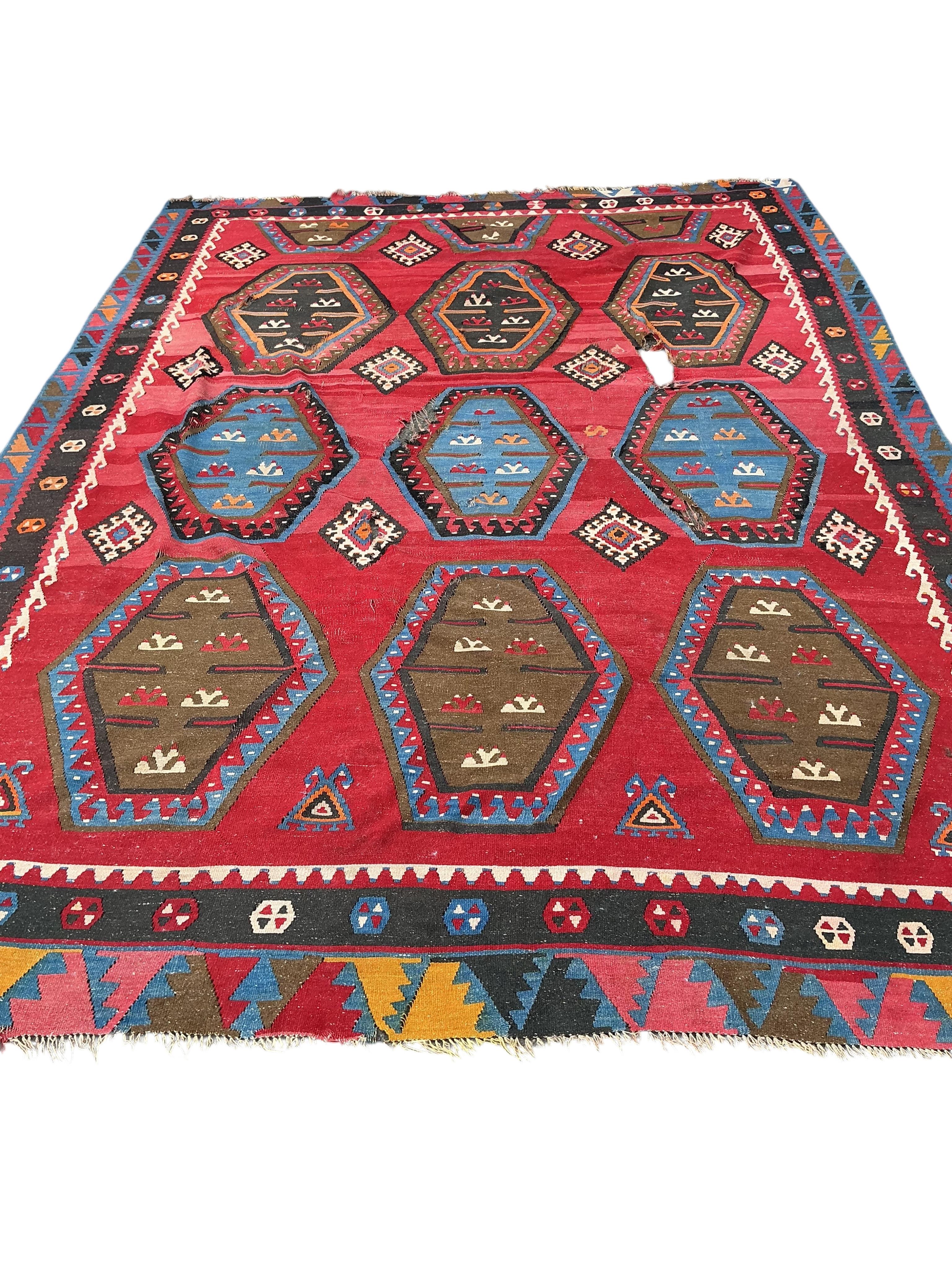 A Turkish Kilim flatweave polychrome carpet, woven with three rows of hexagons, on a red ground, (severely holed and damaged in places), 373 x 267cm